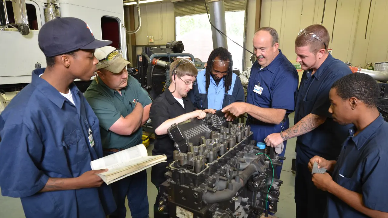 by TSW, Atlanta - Students standing around an engine block as the instructor points to the valve cover